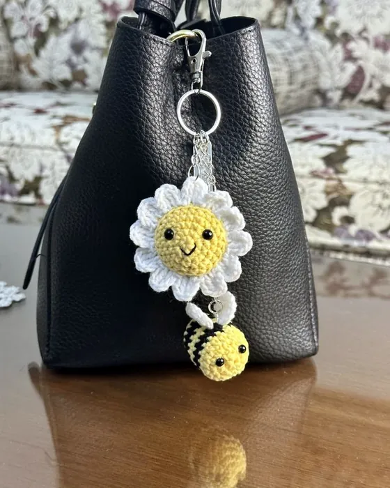 A crocheted daisy keychain with a small bee